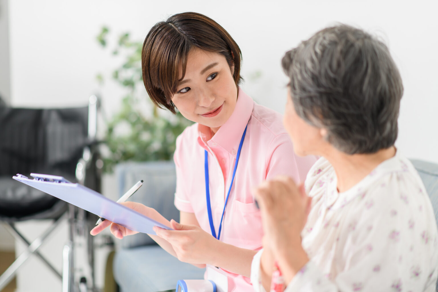 介護職員が高齢者に対応・説明している様子。受付やロビーと思われる明るい室内。