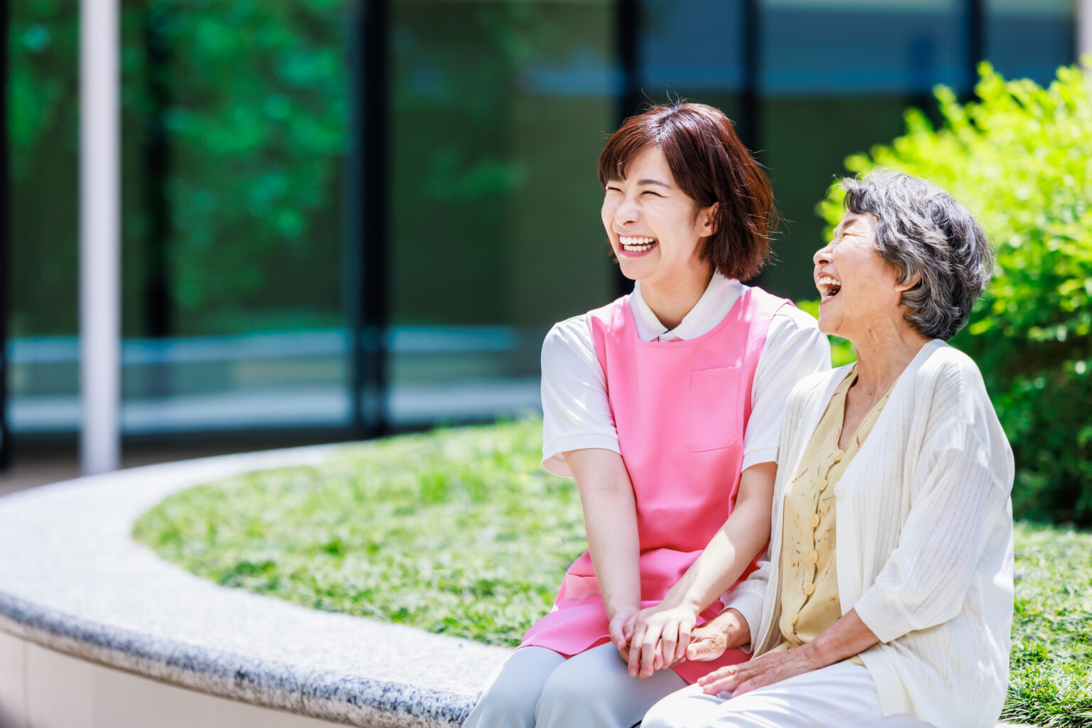 介護職員と入居者が庭で談笑する様子。アクティビティや交流の風景。